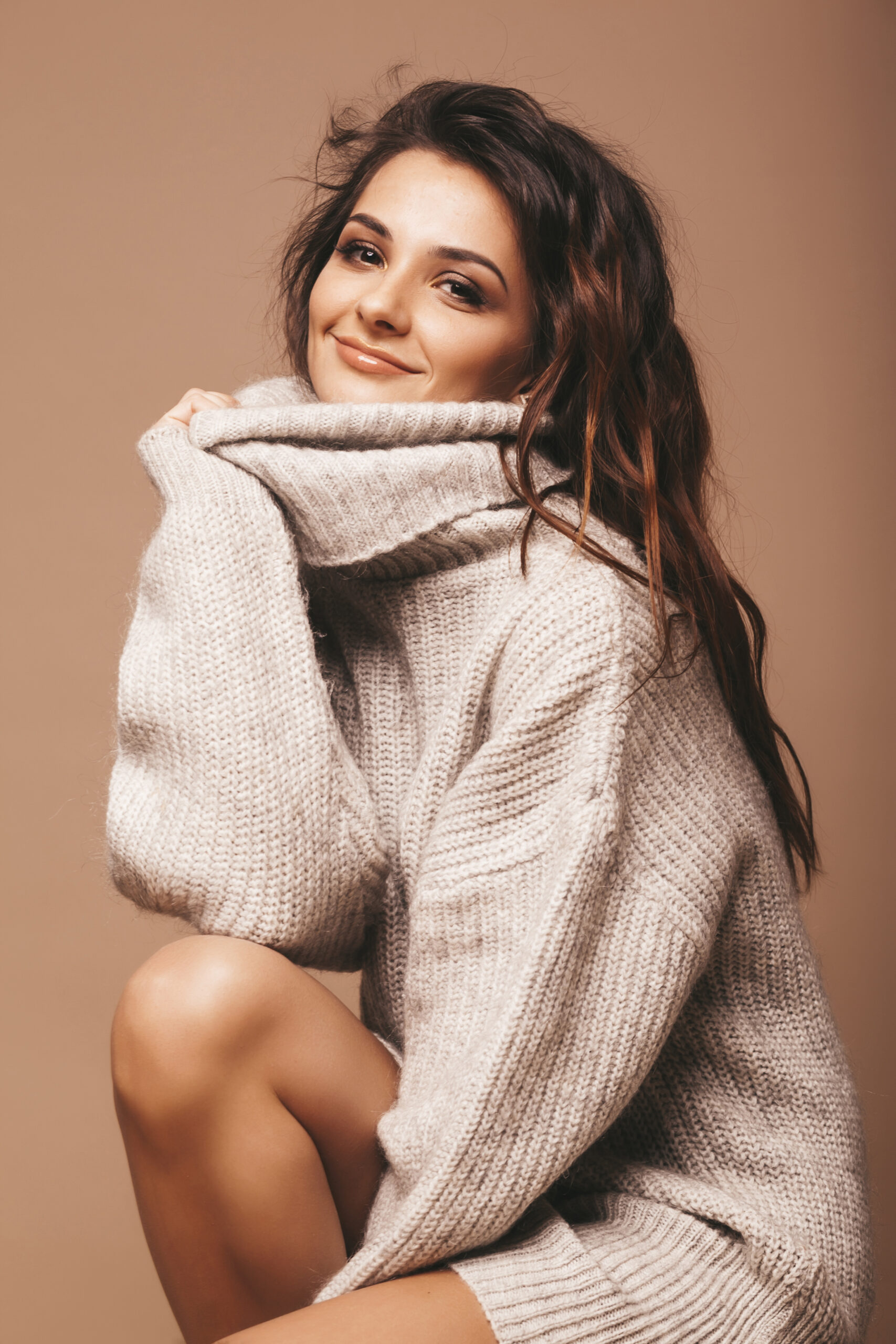 portrait of beautiful sweet cute smiling brunette woman. Girl in casual gray sweater. Model posing in studio. Sitting on chair